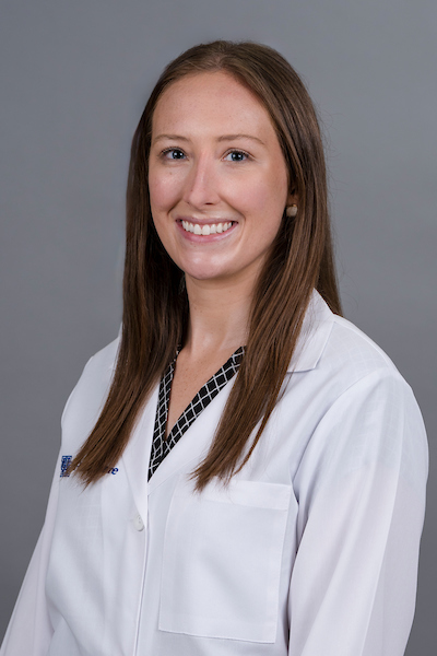 A woman in a white lab coat smiles for a headshot. She has medium length, straight brown hair