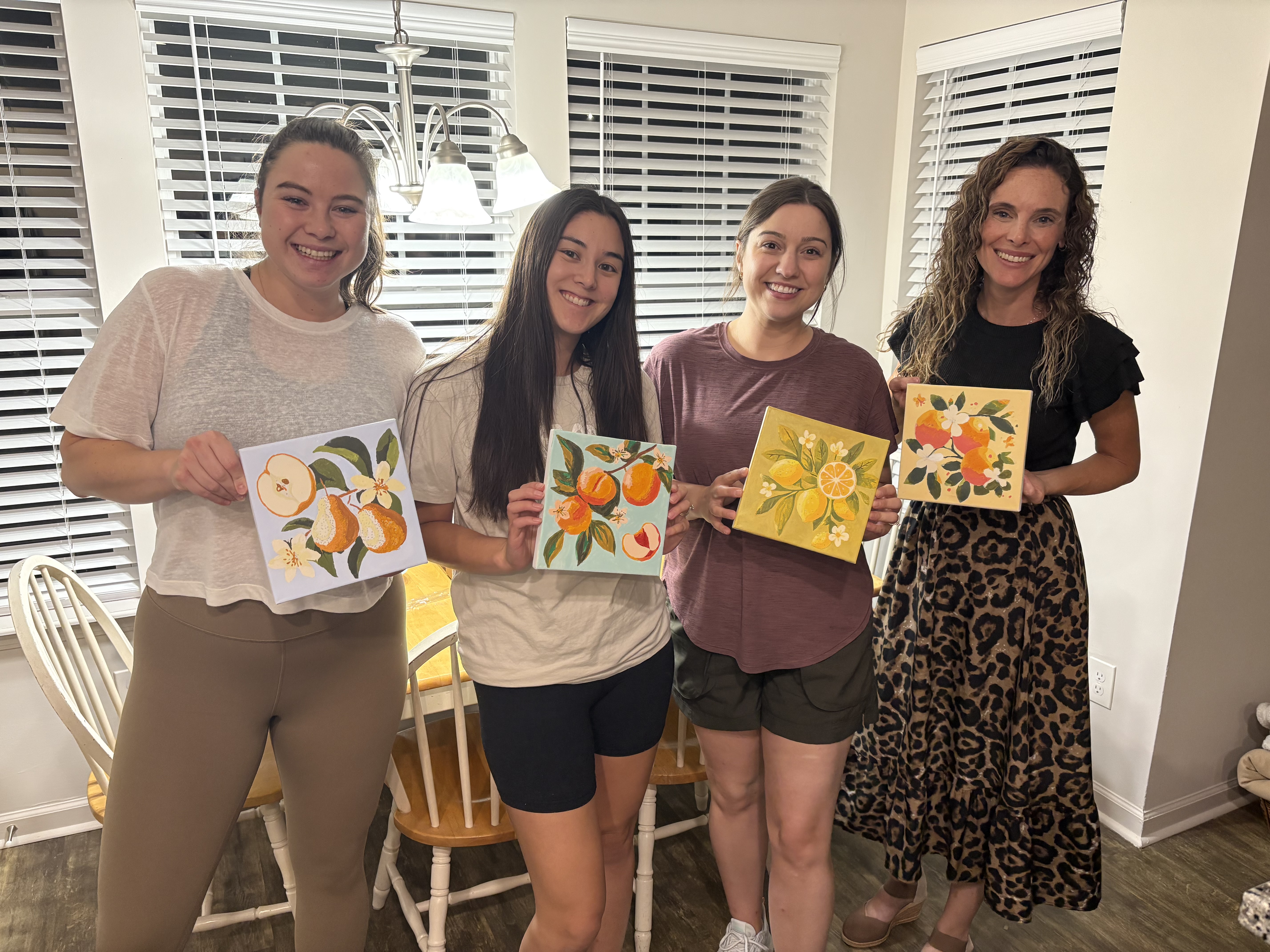 Madison Han Connely and three friends holding up hand-painted illustrations of fruits.