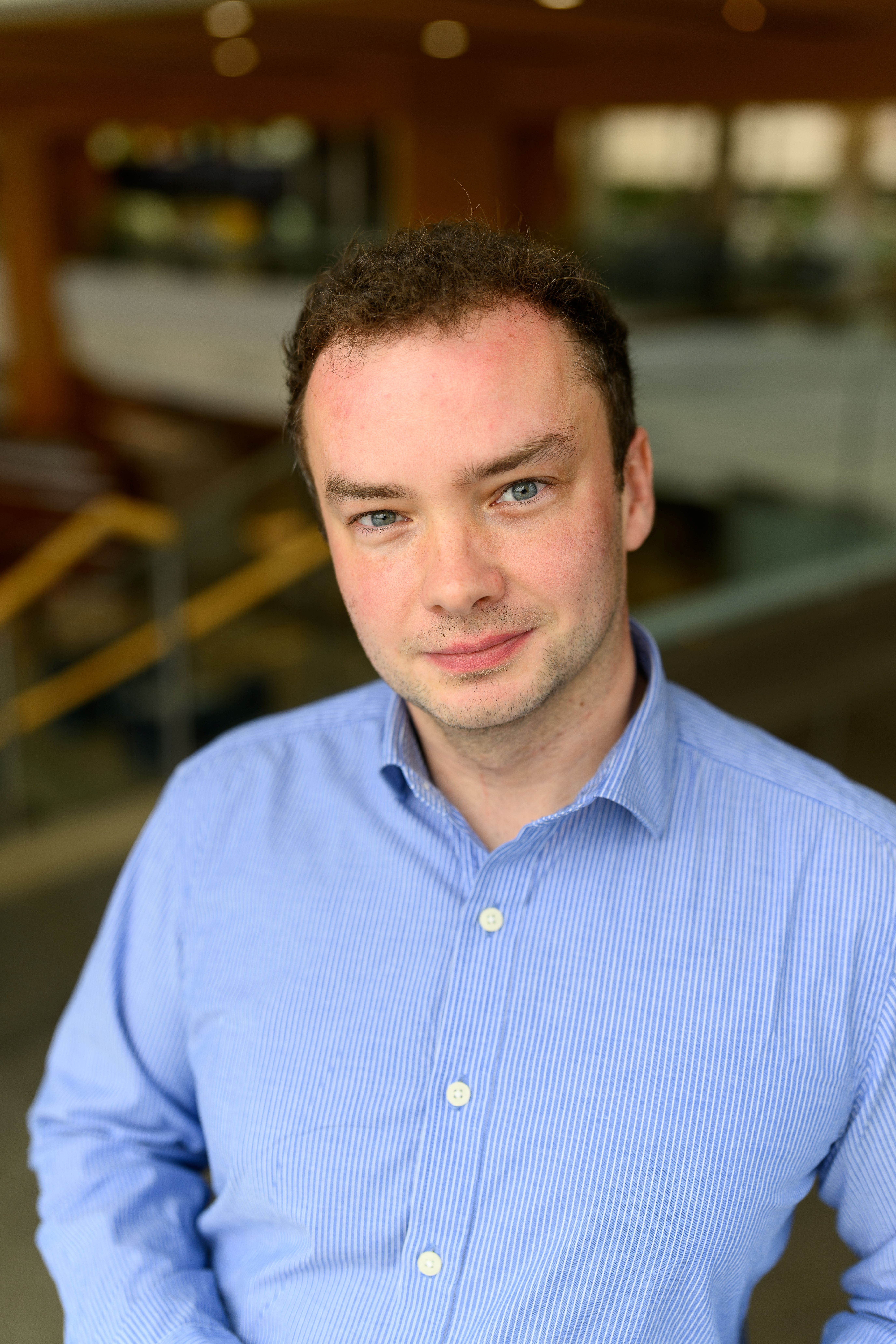 A man poses for a headshot in a blue collared shirt