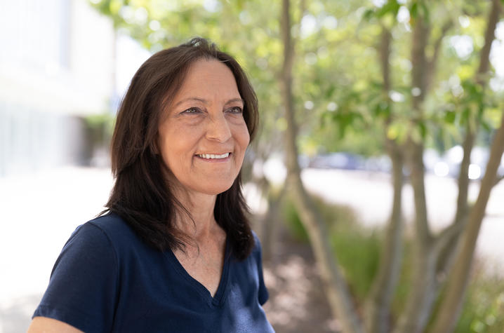 Lisa Buede, a woman with dark, shoulder-length hair and wearing a navy shirt, sitting outside in front of a tree on UK's campus.
