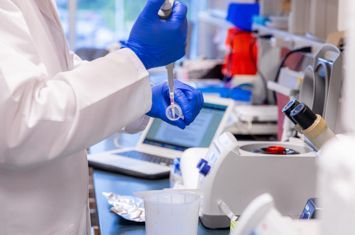 A close up of a lab worker, wearing blue gloves, and prepping a pipette for a centrifuge.