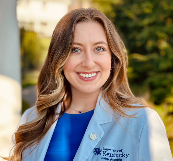 Portrait of Chloe Embry, wearing a blue blouse under a white coat embroidered with UK College of Medicine logo