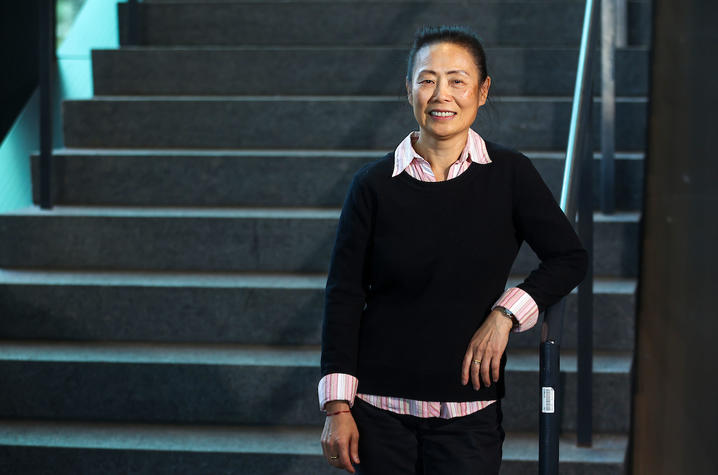 Dr. Wang stands at the bottom of a staircase, wearing a black sweater. 