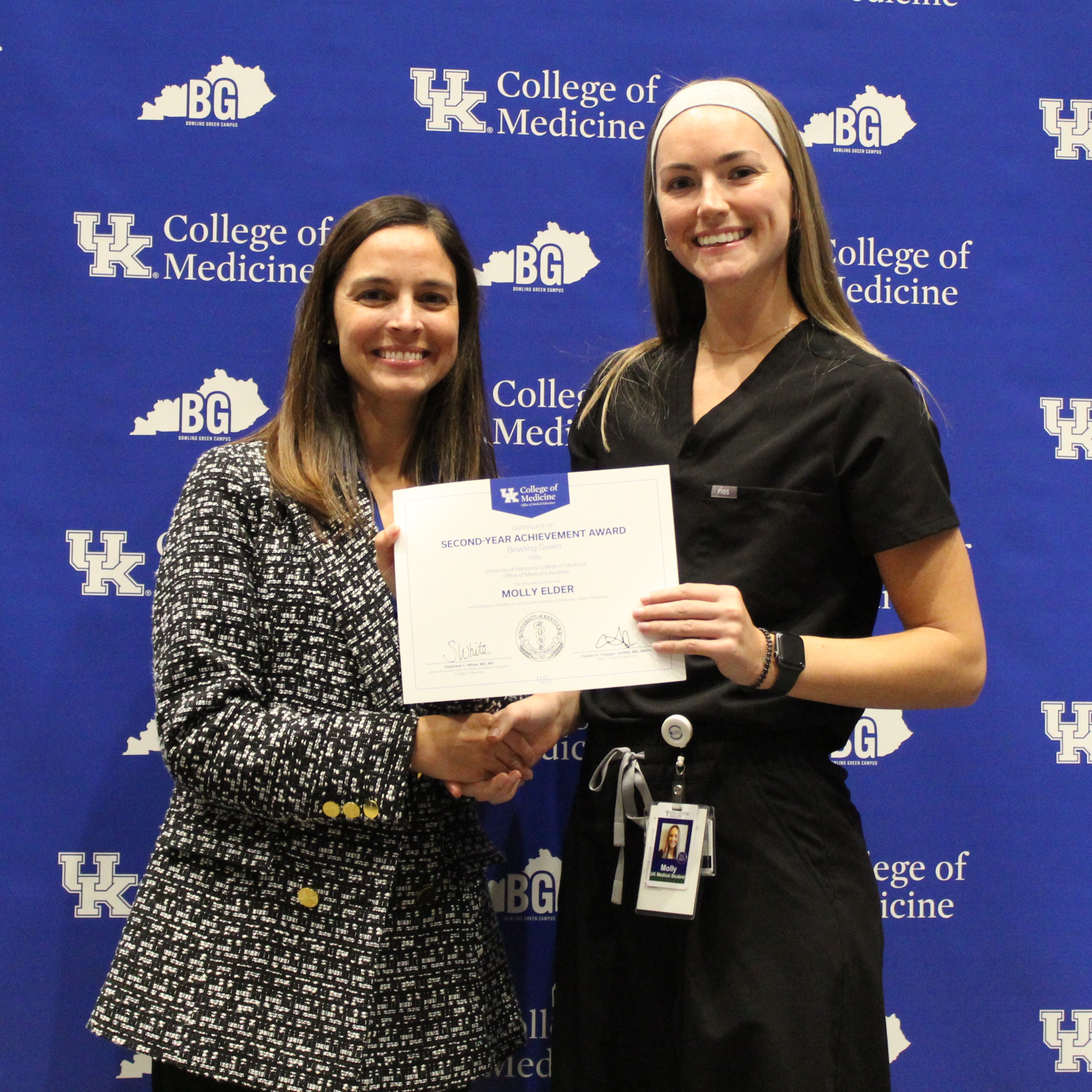 Awardee and presenter hold a certificate and pose for a photo in front of blue backgroudn