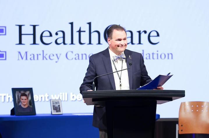 John D'Orazio, MD standing in front of a UK HealthCare Markey Cancer Foundation banner, giving a presentation at a podium.