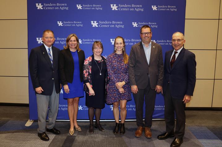 From left: Britt Brockman, Kentucky Sen. Amanda Mays Bledsoe, Linda Van Eldik, Mallory Martinez, Kentucky House Majority Floor Leader Steven Rudy and Eli Capilouto standing in front of a Sanders-Brown Center on Aging banner wall.