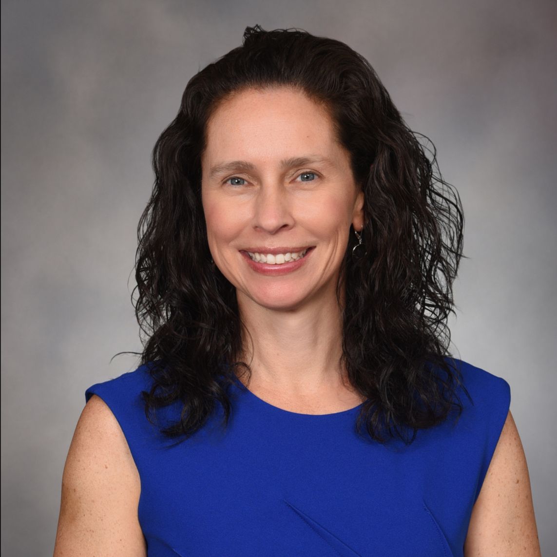 Portrait photo of a woman with shoulder-length brown hair wearing a royal blue sleeveless blouse