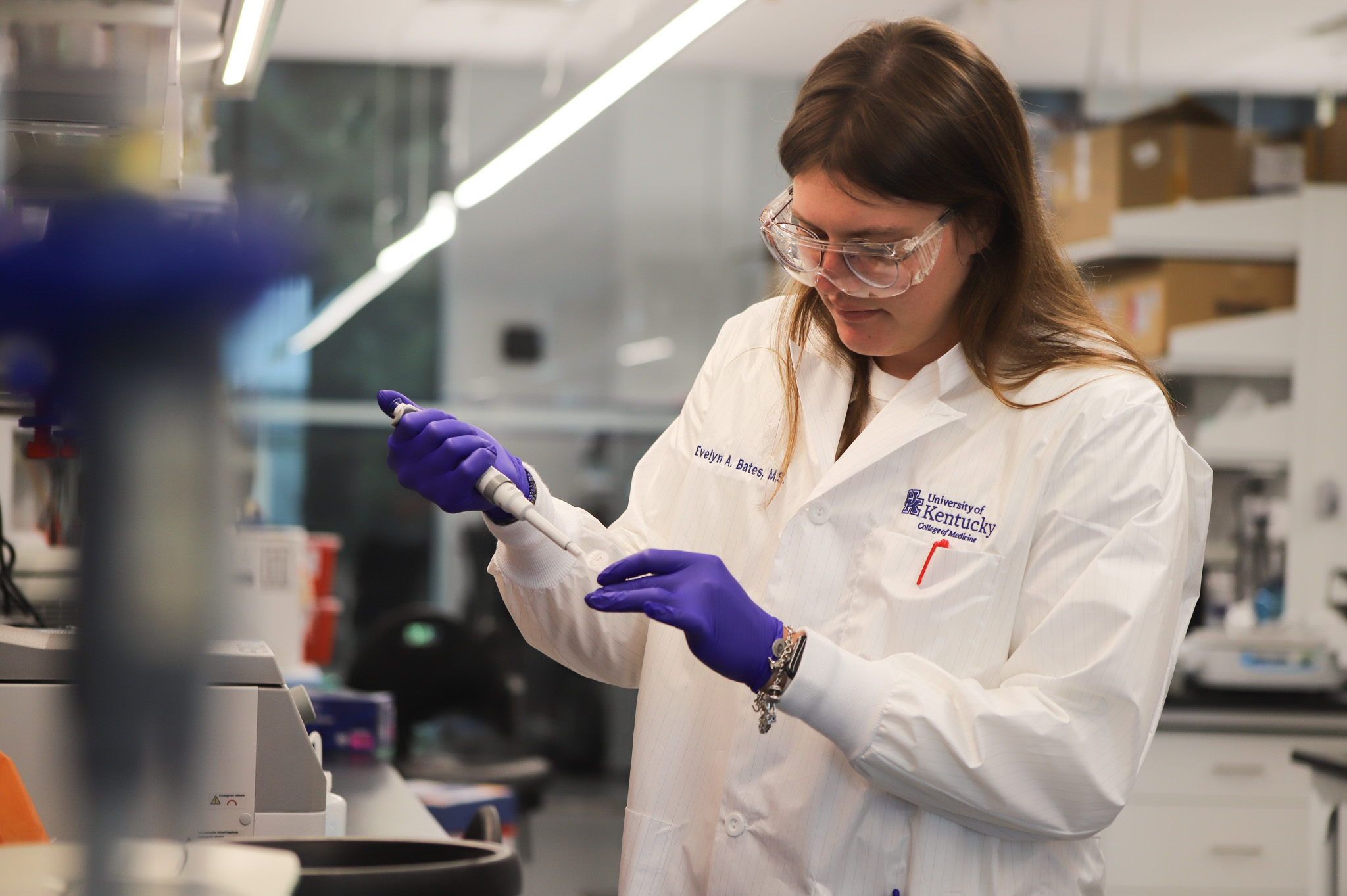 Evelyn, a young woman in white coat and purple gloves, conducting research in a lab