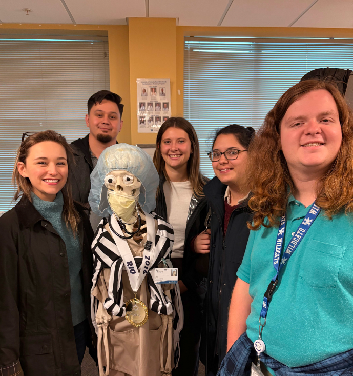 5 medical students pose with a life-size skeleton during a visit to UK COM Morehead Campus