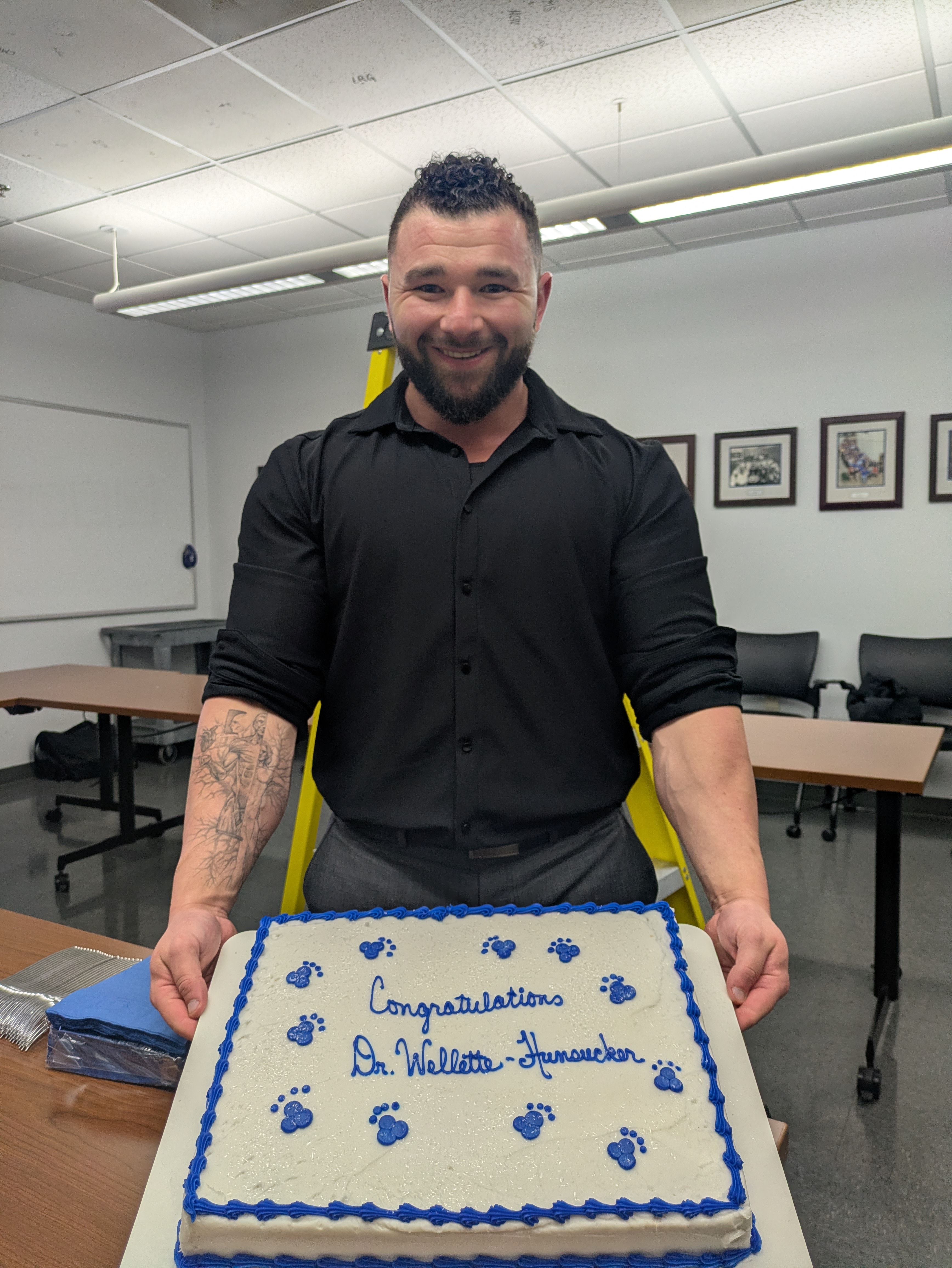 Picture of Dr Wellette-Hunsucker holding a cake that says, "Congratulations Dr. Wellette-Hunsucker".