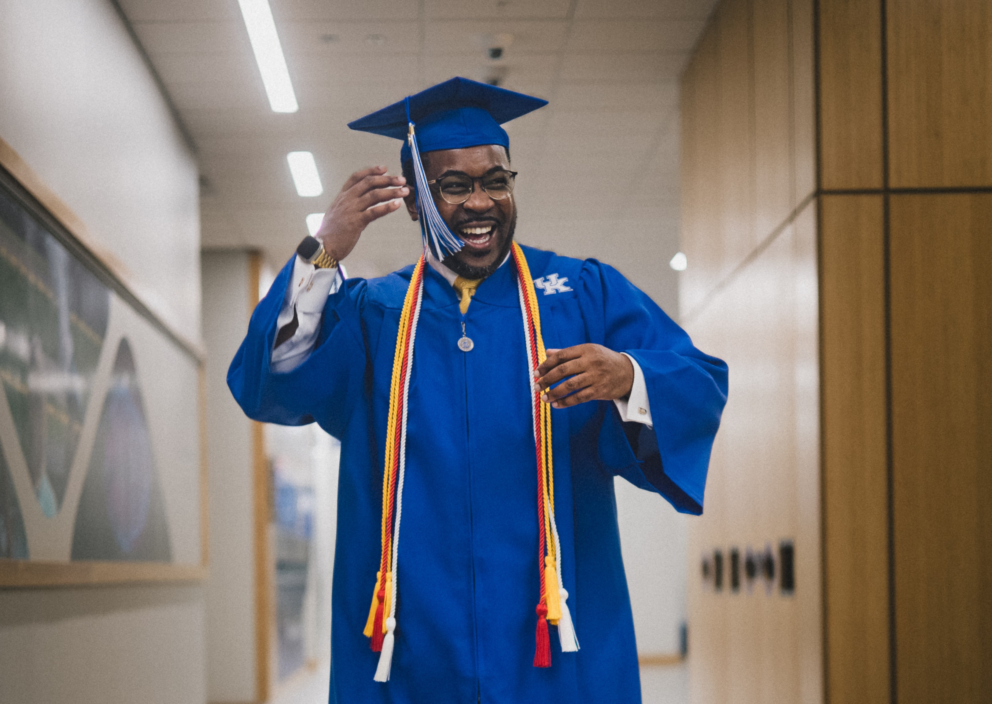West poses in UK regalia (blue cap, gown, multi-colored cords)