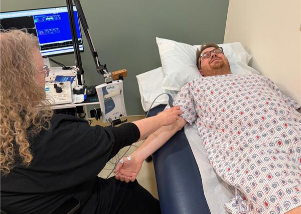 Man lying on a medical examination table in a patterned gown, while a healthcare professional conducts a test using medical equipment. The room is clinical, conveying a calm atmosphere.