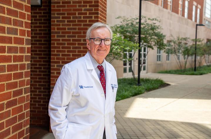 Dr. Phil Tibbs wearing white coat stands in front of brick building for photo