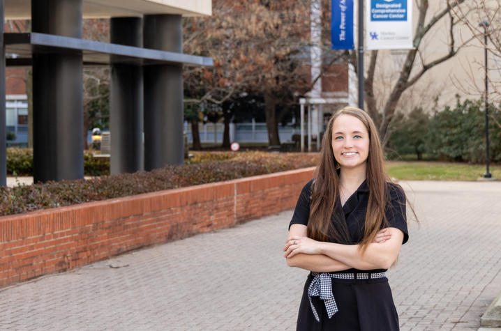 Gabby Morrison in a black dress, standing on UK's campus with her arms crossed.