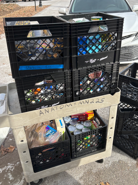 Crates of canned and other non-perishable food collected on a beige wheeled cart to donate. 