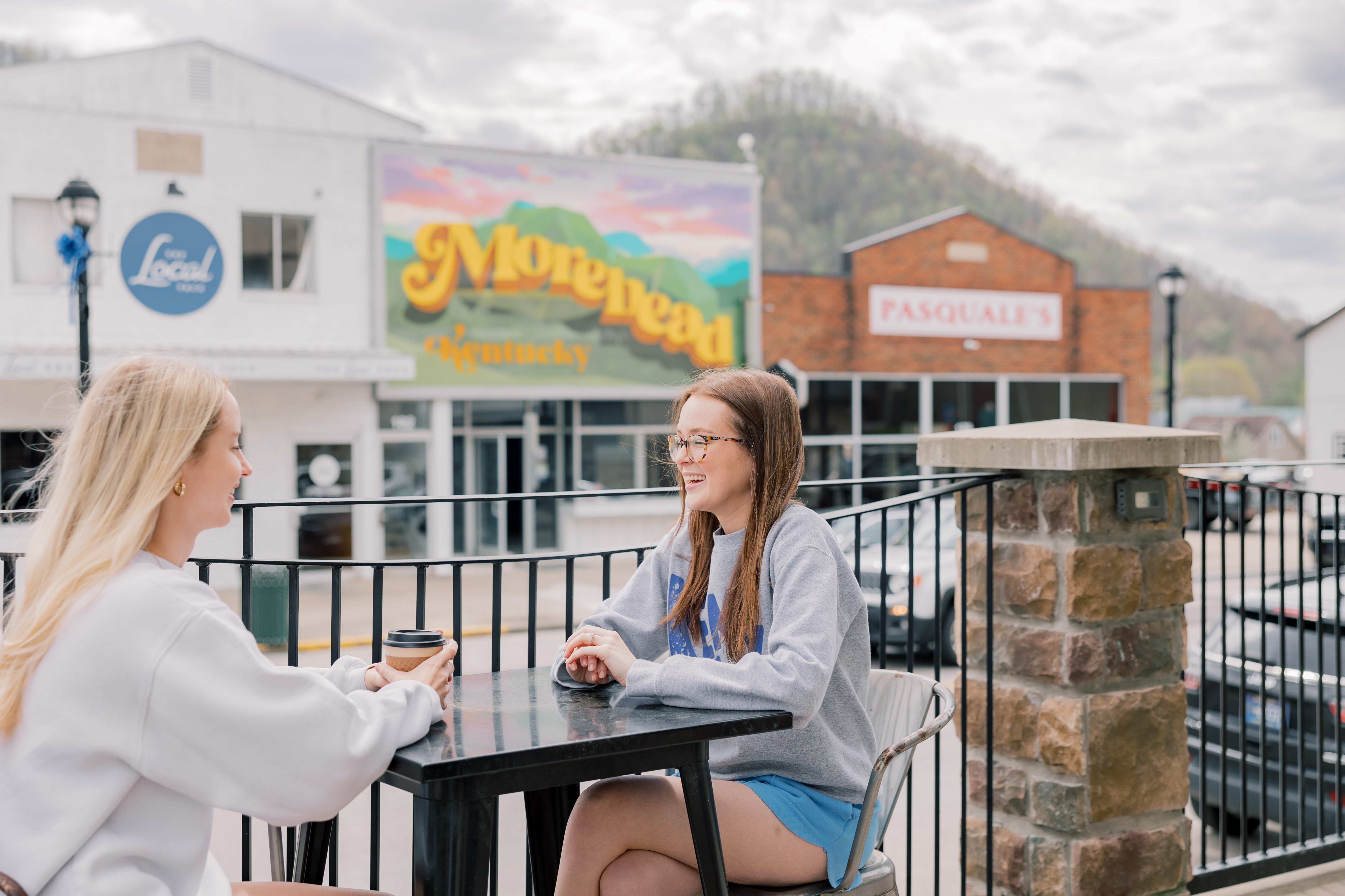 two students sitting outside having coffee together in downtown morehead