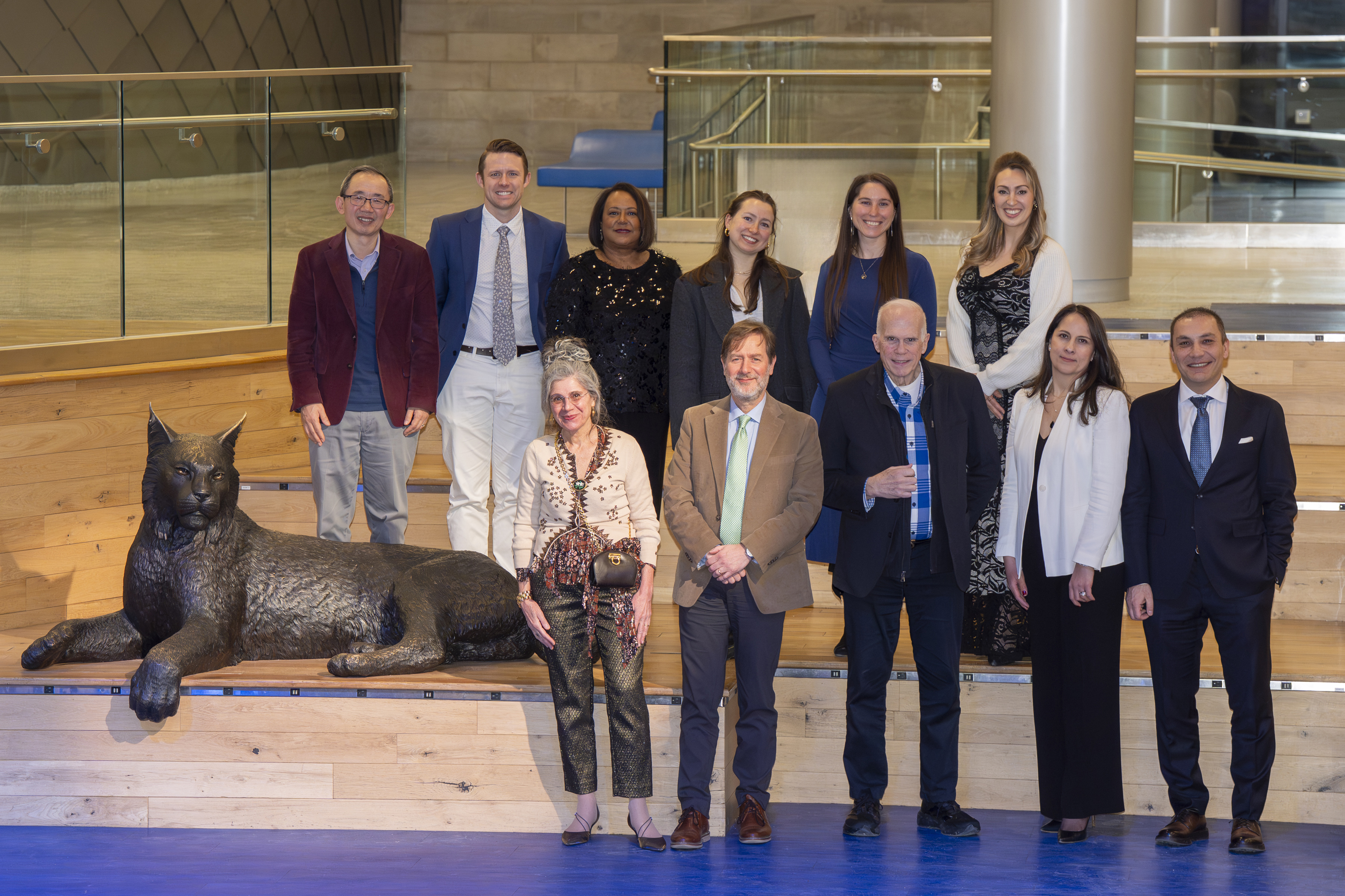 A group of people stand in formal attire next to a metal statue of a wildcat
