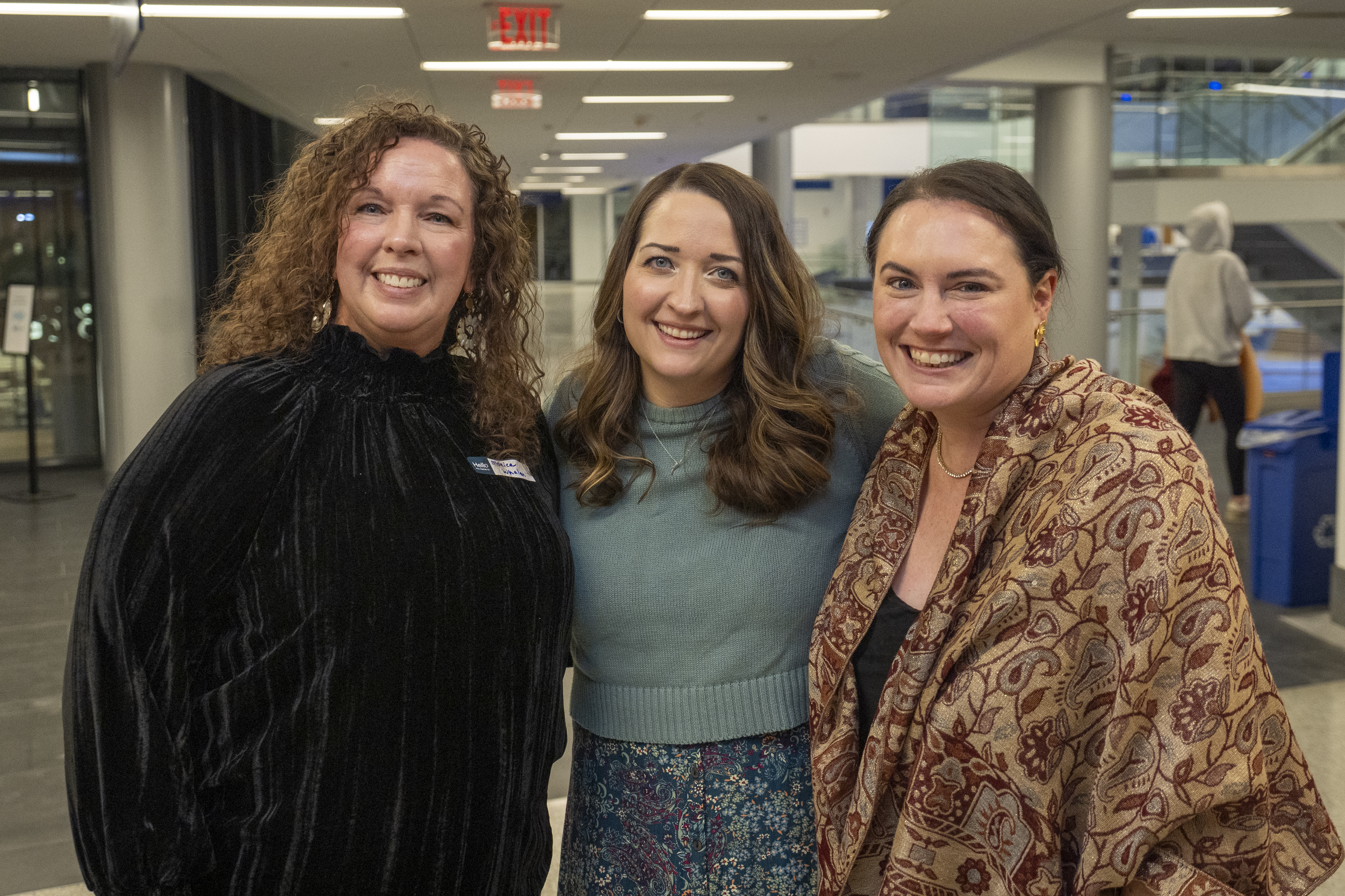 Three women in formal attire smile for a photo together