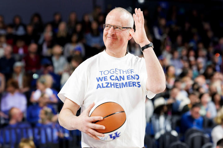 Peter Nelson stands on the UK basketball court, holding a UK basketball and wearing a white shirt that reads, "Together we can end alzheimer's"