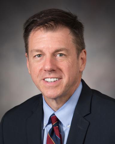 headshot of Dr. Jay Grider, wearing a suit and tie in front of a gray background