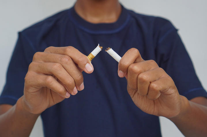 A person in a blue t-shirt snapping a cigarette in half.