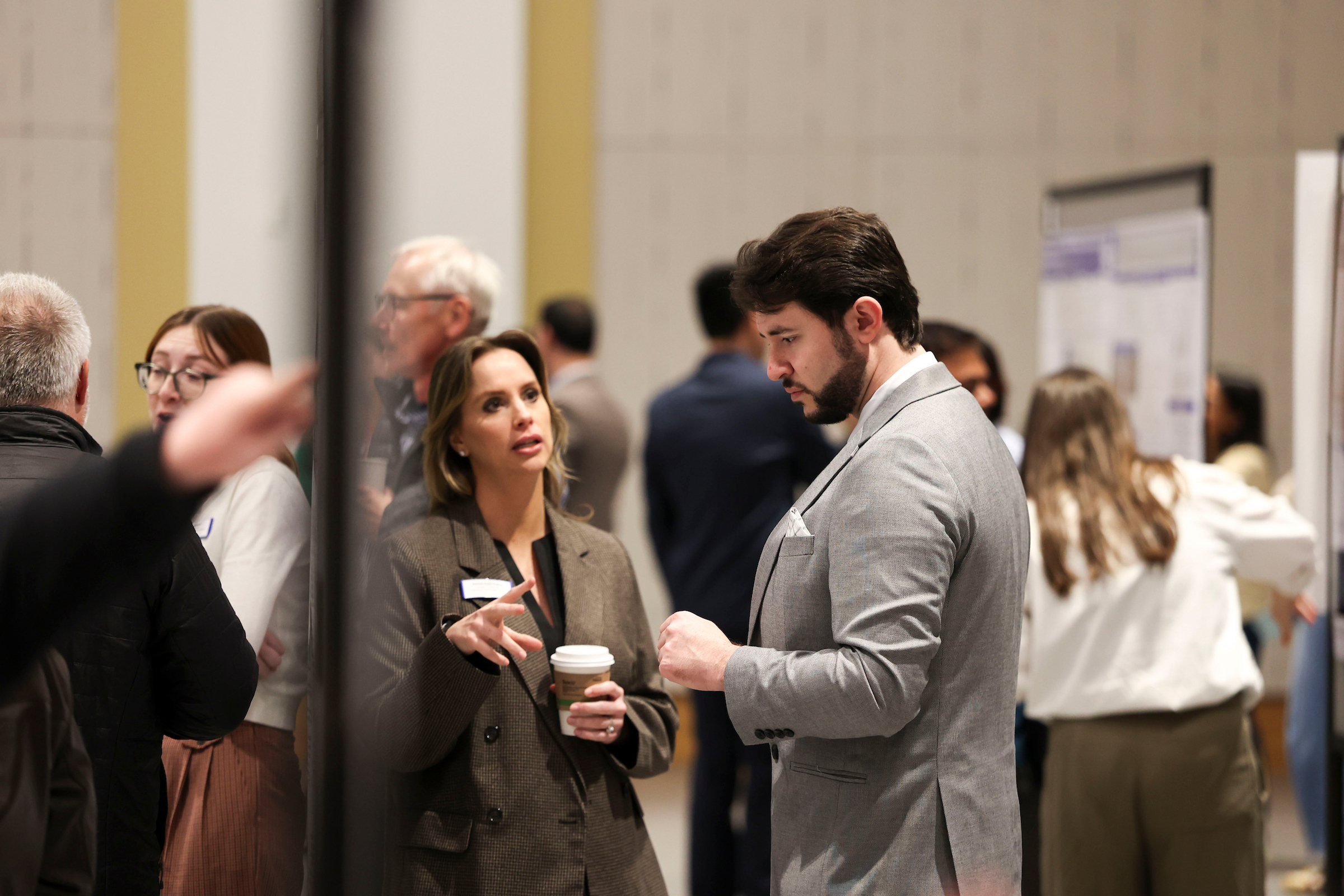 Two attendees talk during a research poster session while other guests mingle and view posters in the background.