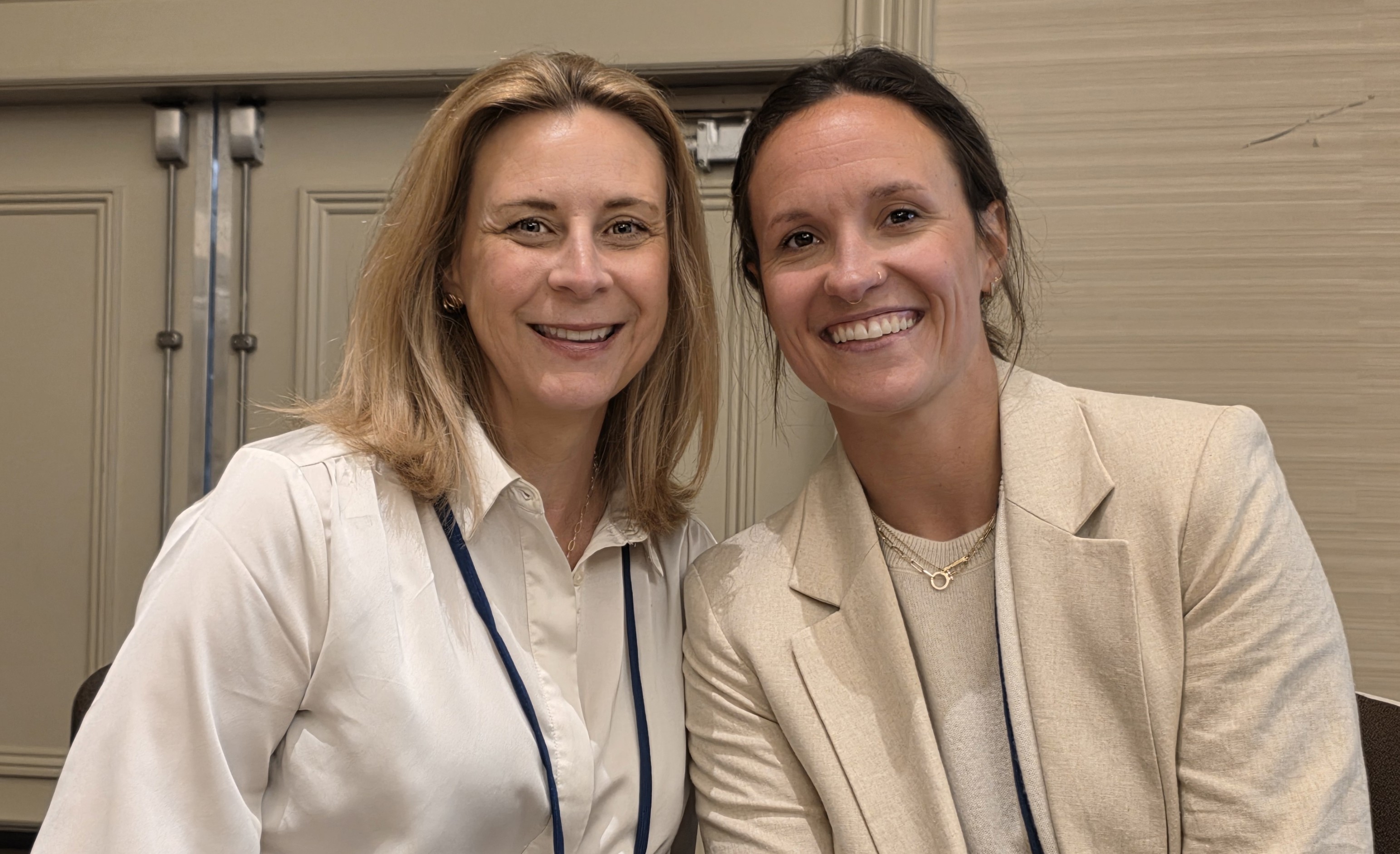 Two women in cream colored blouses smiling seated together
