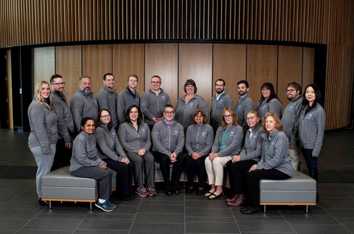 The RADOR-KY research team in matching grey jackets. They are gathered in two, overlapping  semi-circles, with the front row sitting down, and the back row standing.