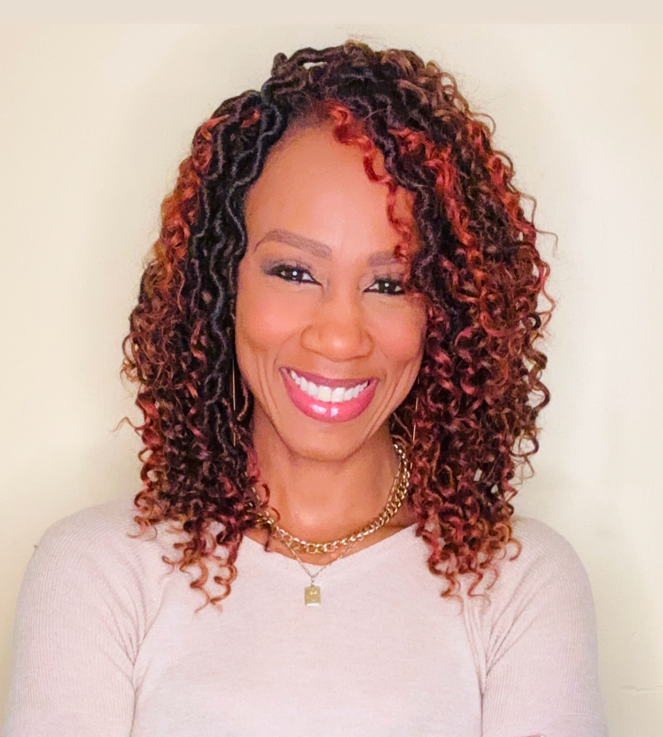 Professional headshot of Dr. Ketrell McWhorter smiling at the camera. She has shoulder-length, tightly curled dark hair with auburn highlights and is wearing a light beige top, gold jewelry, and is photographed against a plain cream-colored background