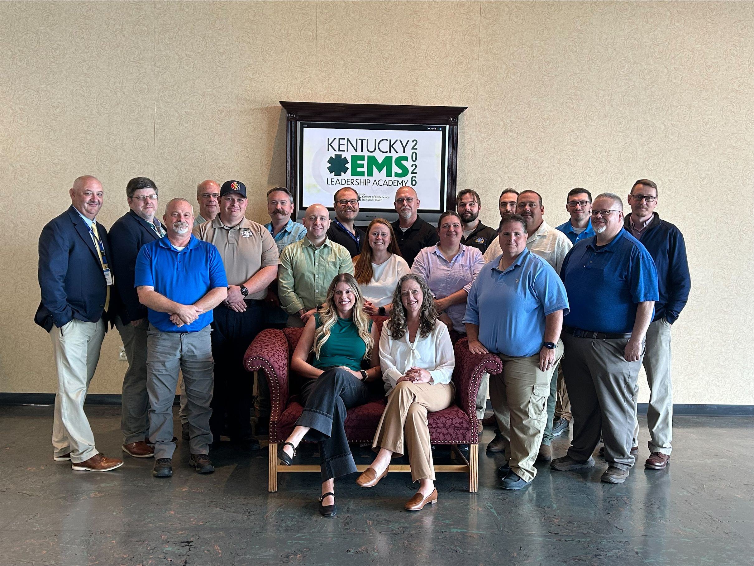 Kentucky EMS Leadership Academy 2026 graduates and mentors pose for a group photo in Kentucky, standing and seated in front of a wall-mounted academy sign displaying the 2026 program name.