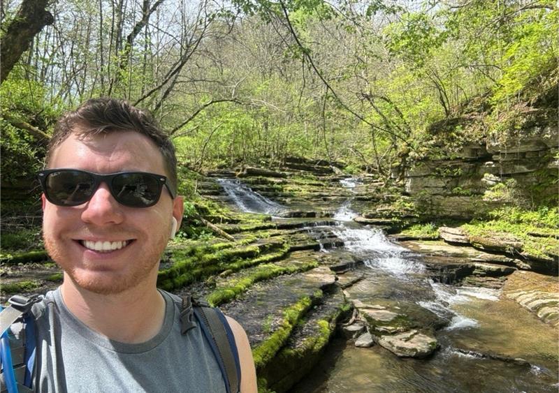 Nick Demas smiling in nature near a stream