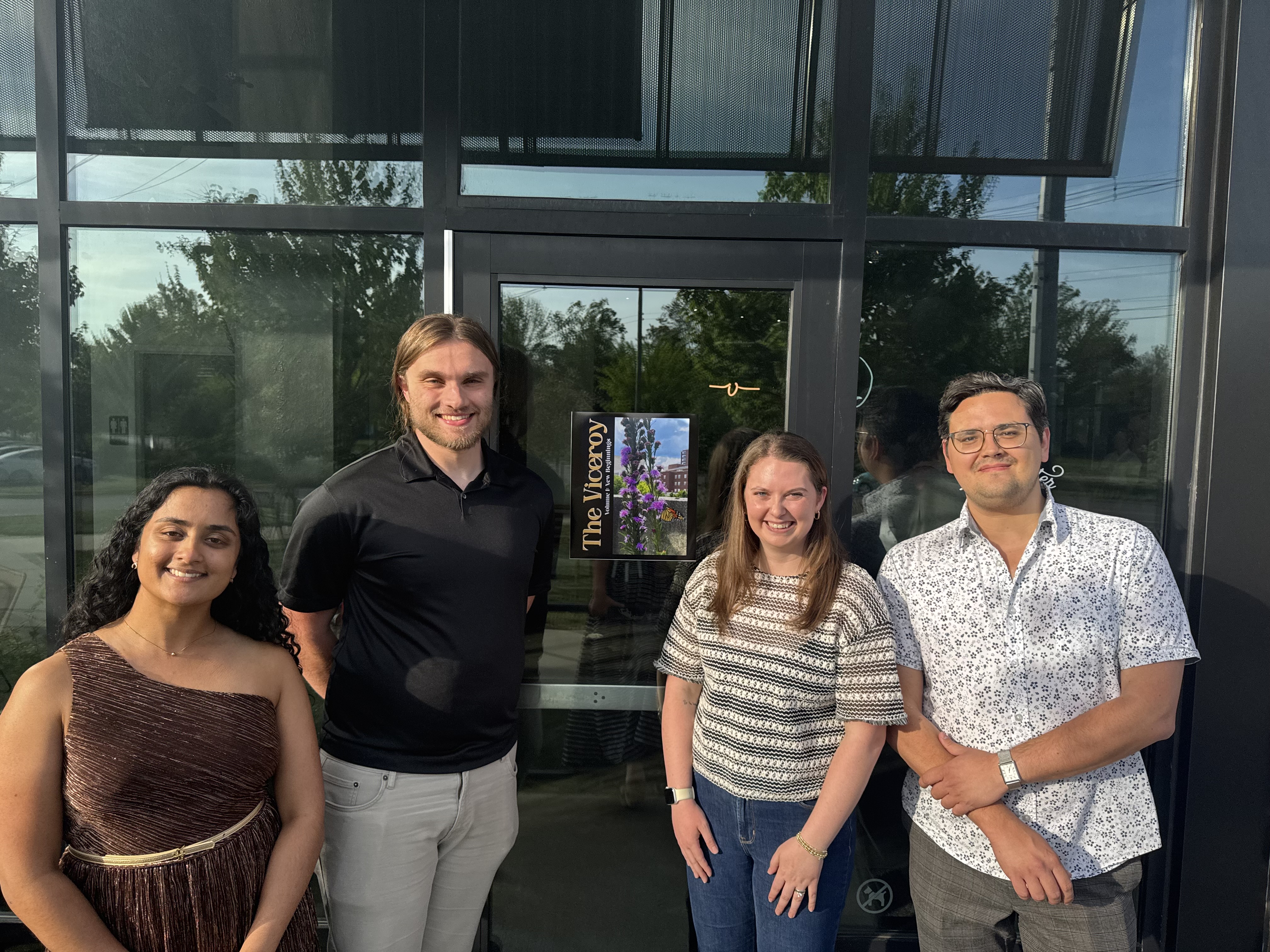 4 Members of the Vitals Group standing outside in front of the magazine cover smiling with arms in different positions.