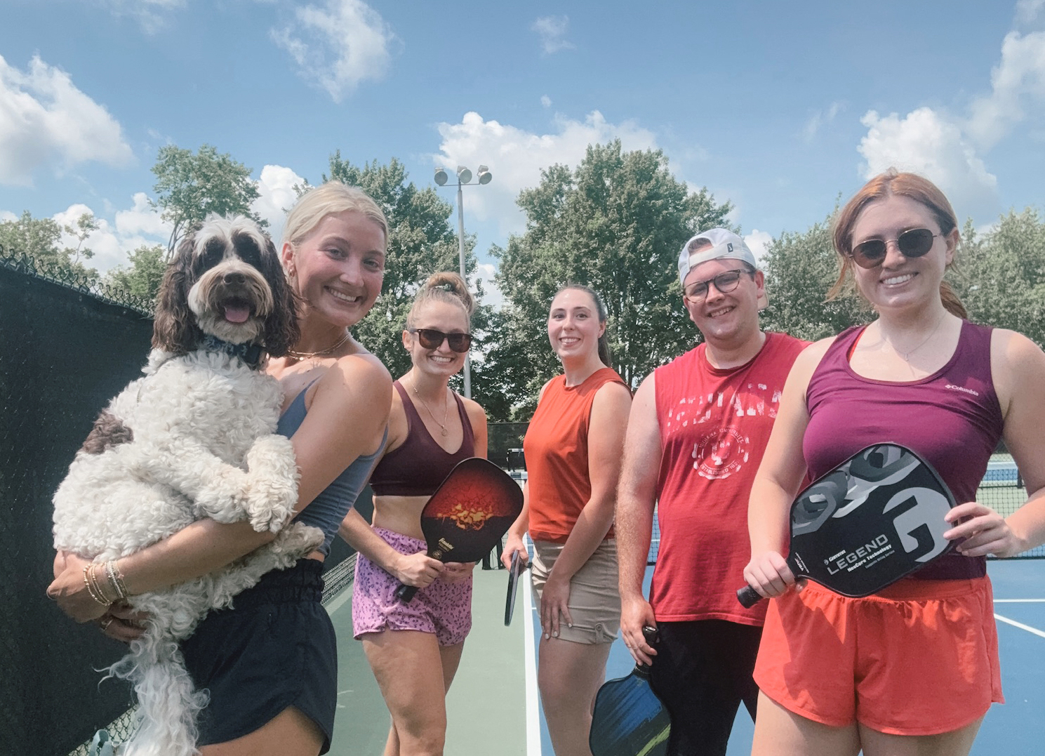 Allie Herron holding her pet doodle, on a tennis court with several friends.