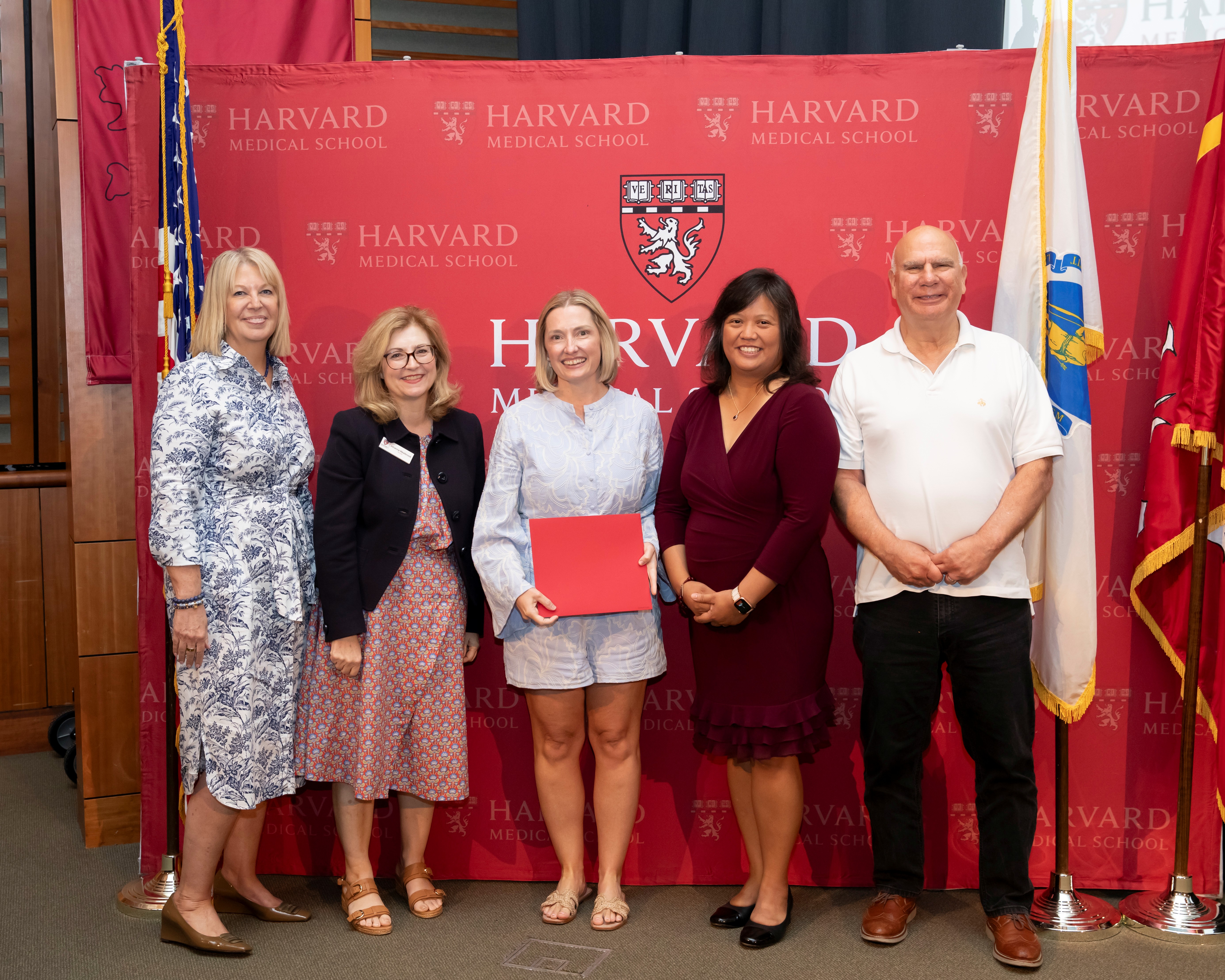 Image of 5 medical professionals at Harvard Medical School's SQIL program graduation with red Harvard College Logo in background. 