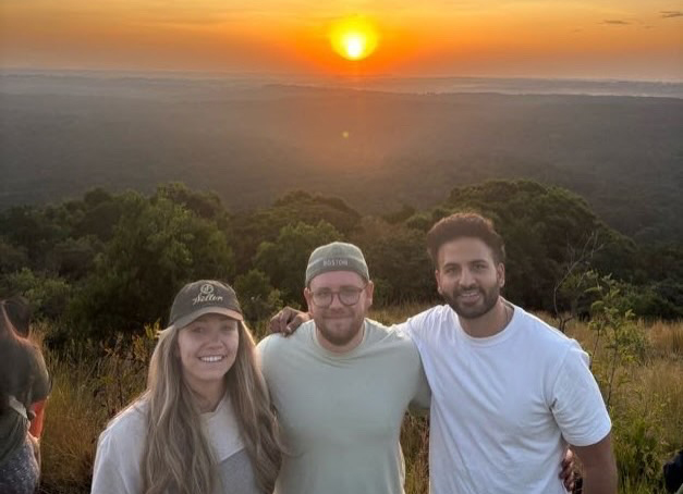Benjamin Fischer and two friends standing together on a hike in front of a setting sun.