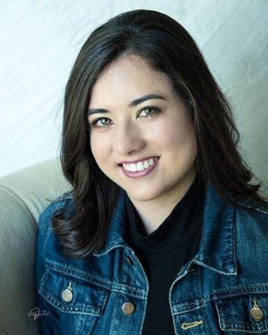Young Caucasian woman with dark hair in a black blouse and jean jacket, smiling