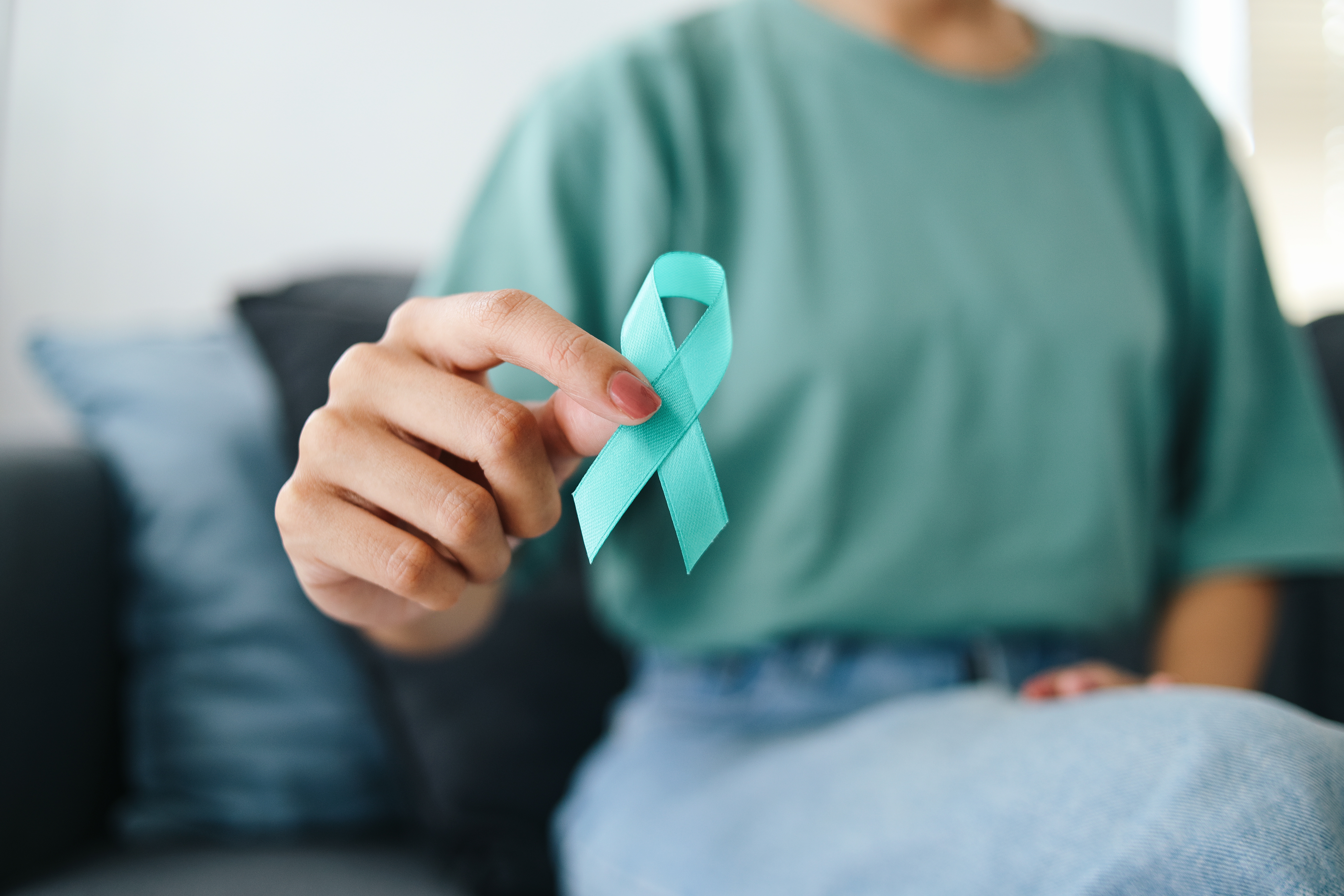 A closeup of a woman's hand, holding an ovarian cancer ribbon