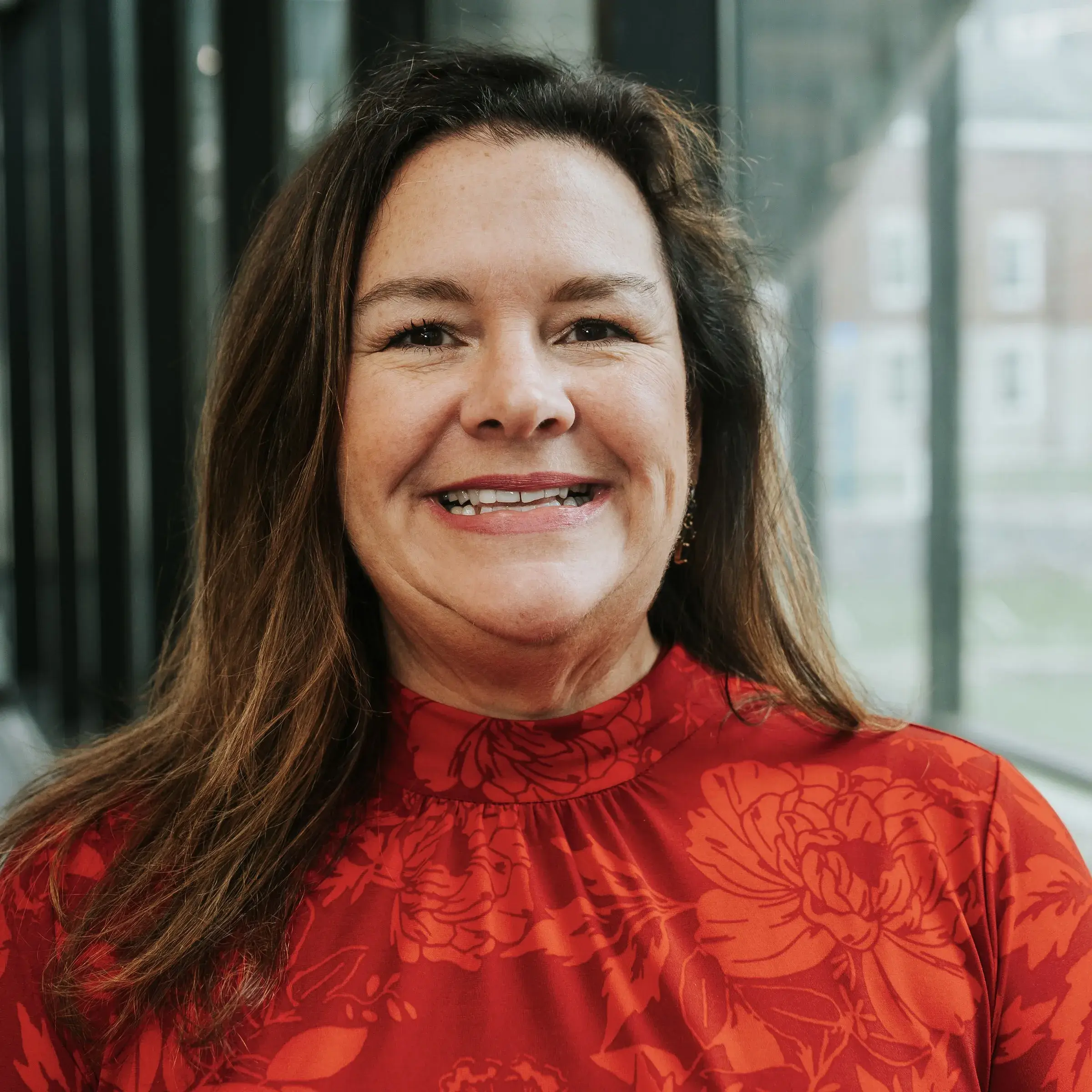 Woman with long brown hair in red blouse, smiling