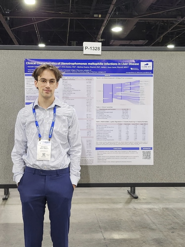 Researcher standing beside a CURE-KY scientific poster titled “Clinical Characteristics of Stenotrophomonas maltophilia Infections in Liver Disease” at a conference poster session.