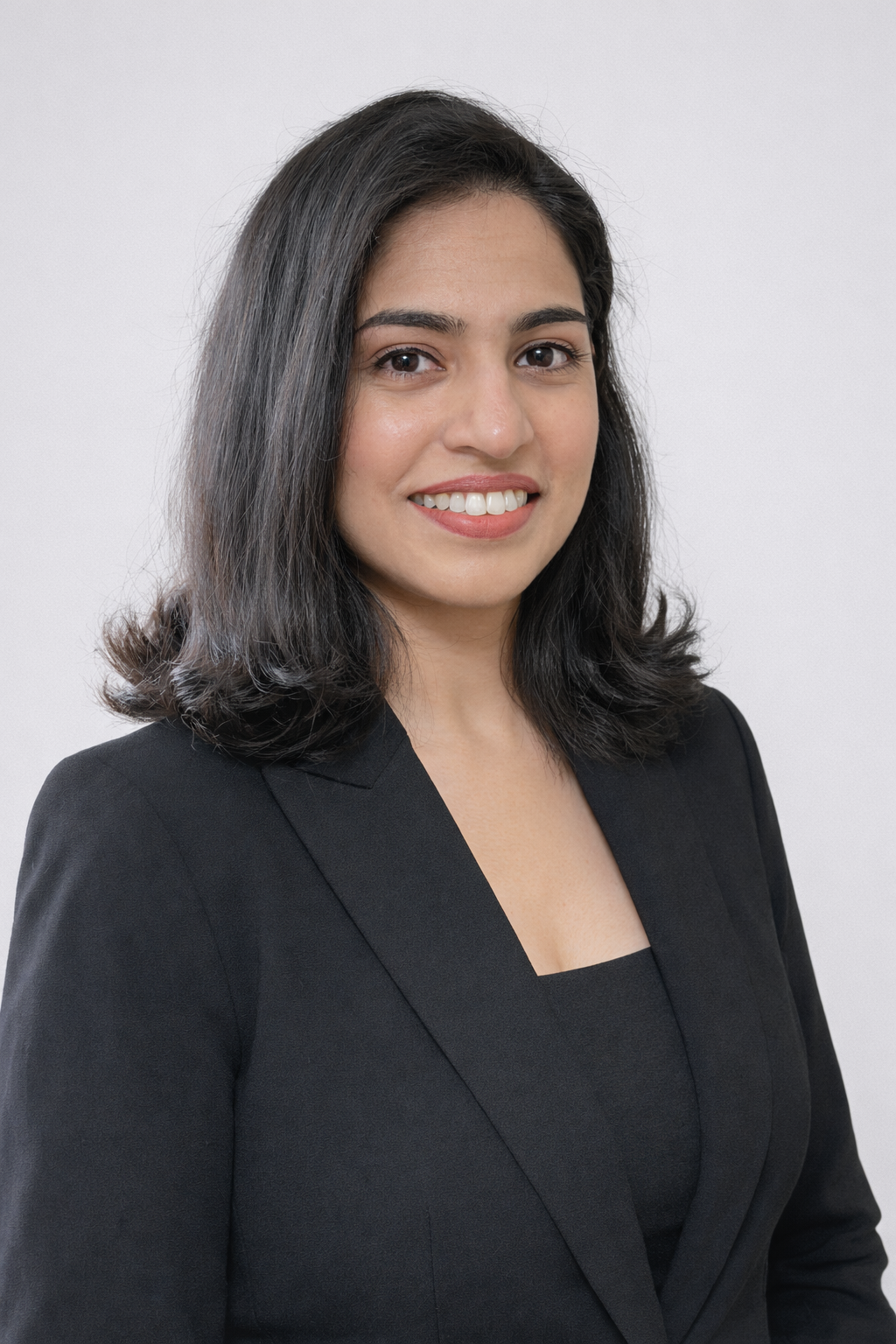 Young woman with dark hair, black blazer and black blouse on white background, smiling