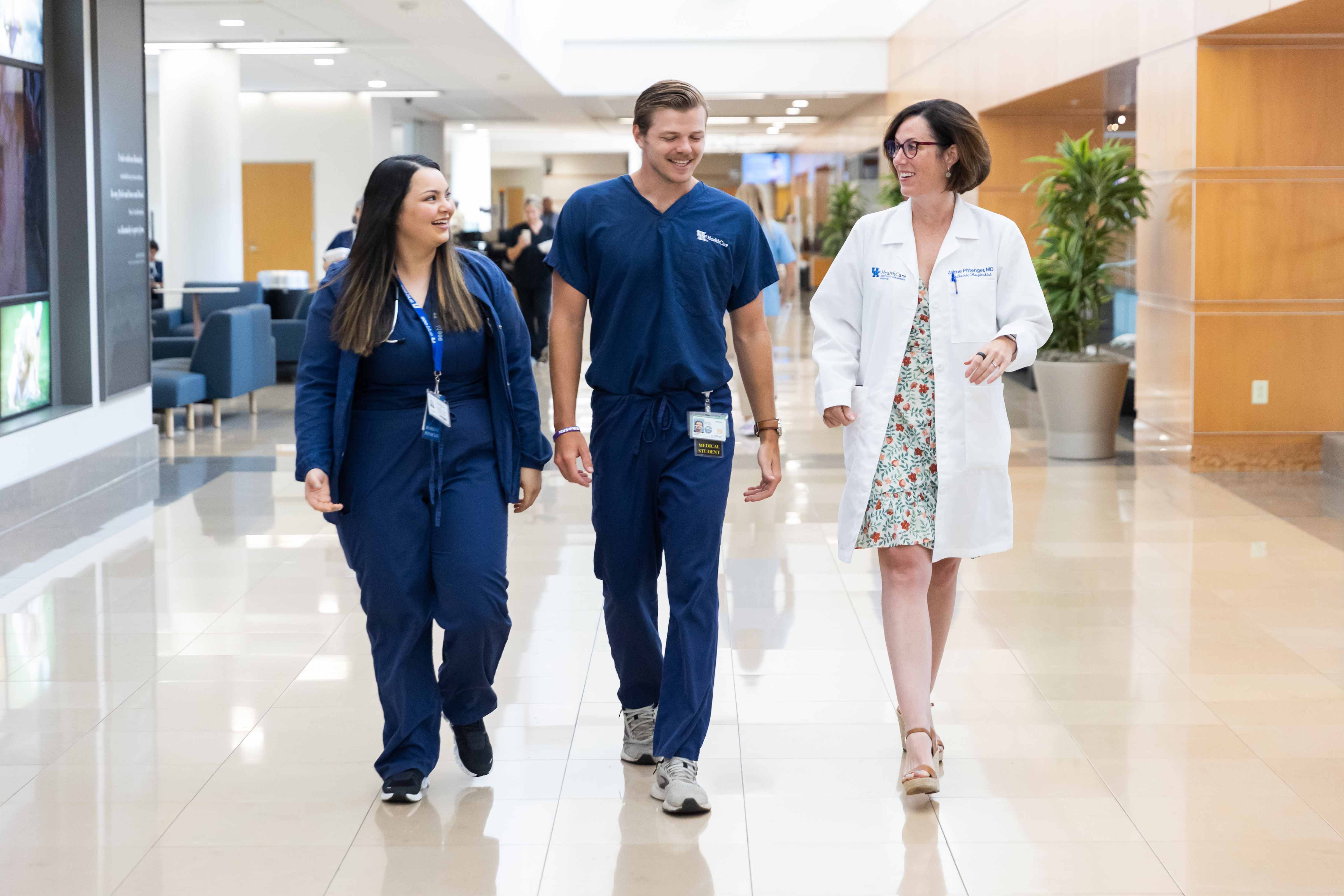 2 medical students in blue scrubs walk alongside an attending in a white coat 