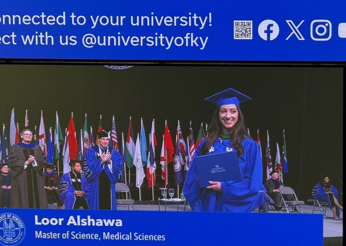 A university graduation screen shows smiling alumna Loor Alshawa in a blue gown and cap, holding her diploma amid international flags; celebratory and proud.