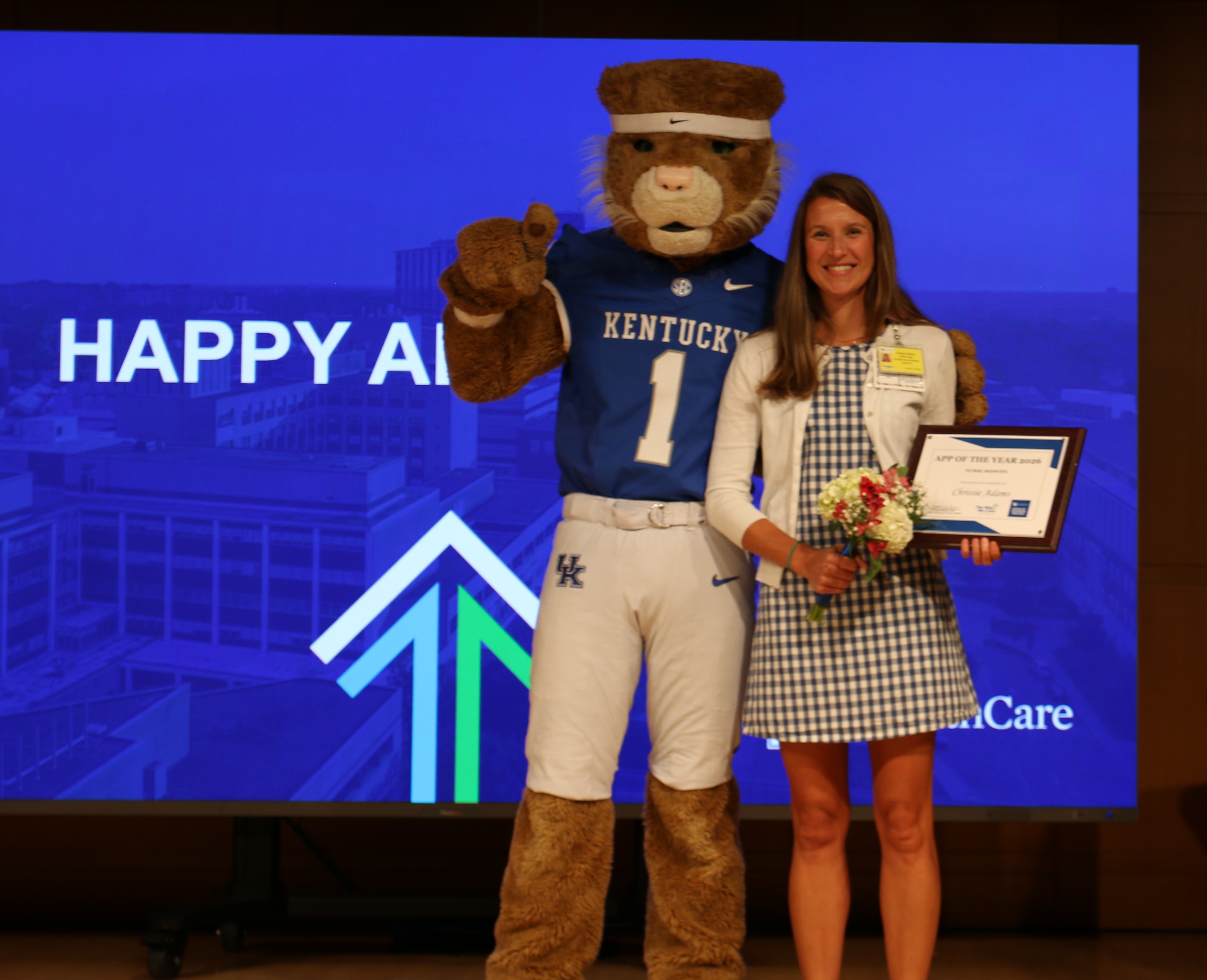 Image of Chrissie Adams, CNM, holding award certificate and posing with Wildcat mascot. 