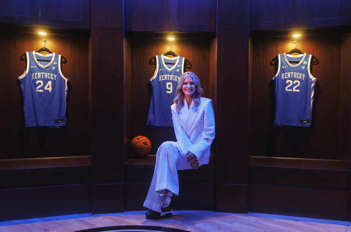 Lee Anne Pope sitting in a dramatically lit room with basketball jerseys hanging behind her on the wall.
