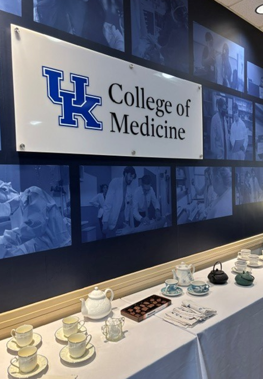 UK College of Medicine sign hangs above a table covered in white table cloth and set for a full tea time. 