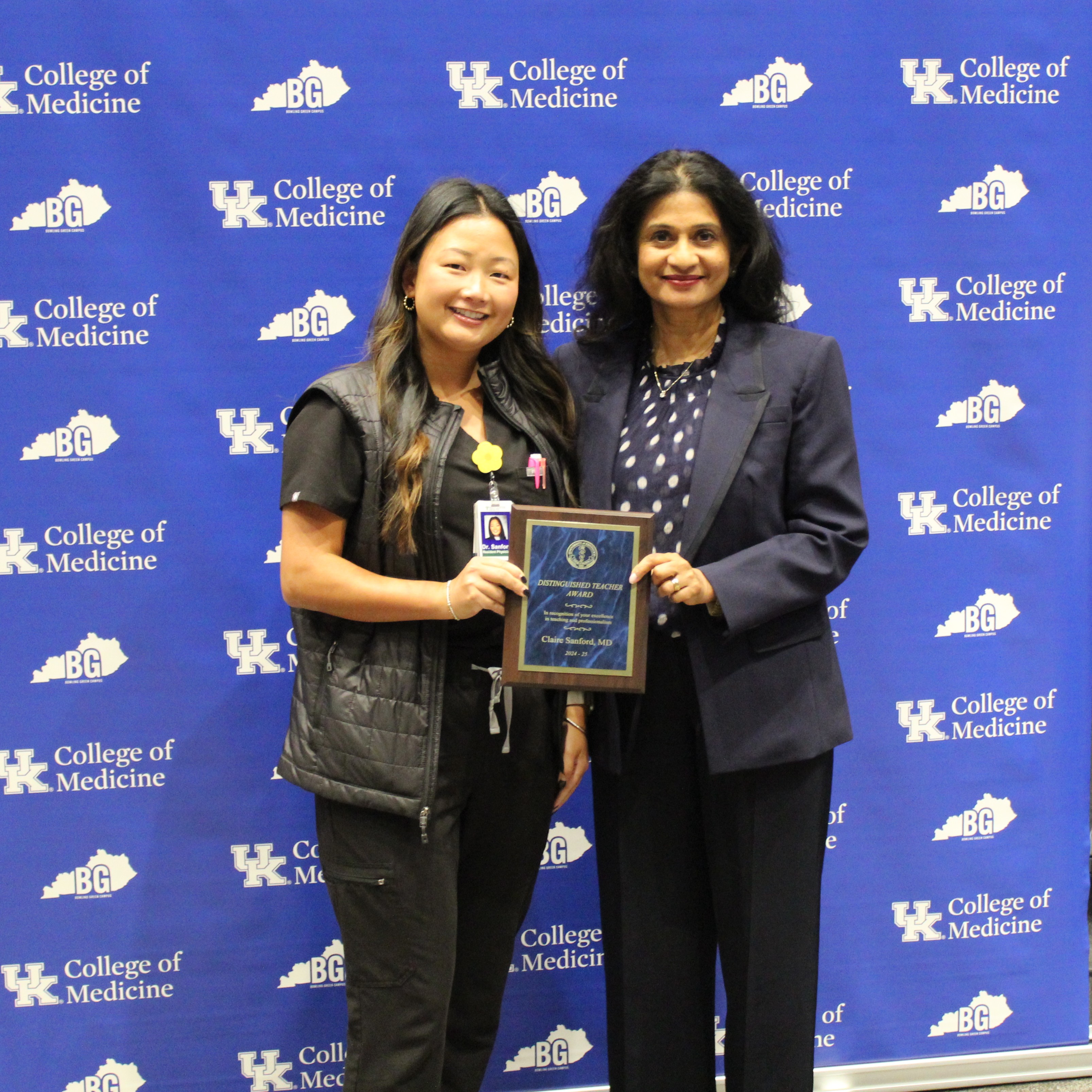 Awardee and presenter hold a plaque and pose for a photo in front of blue backgroudn