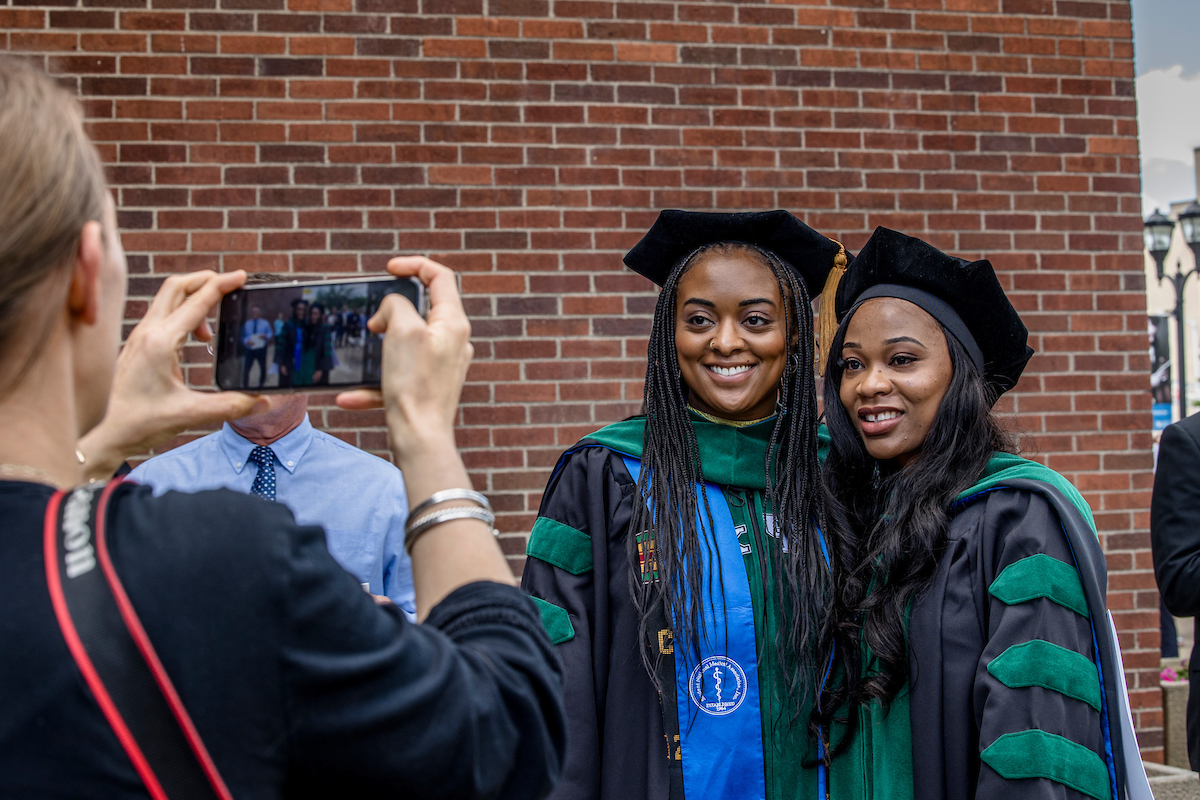 Two graduates pose outside in regalia 