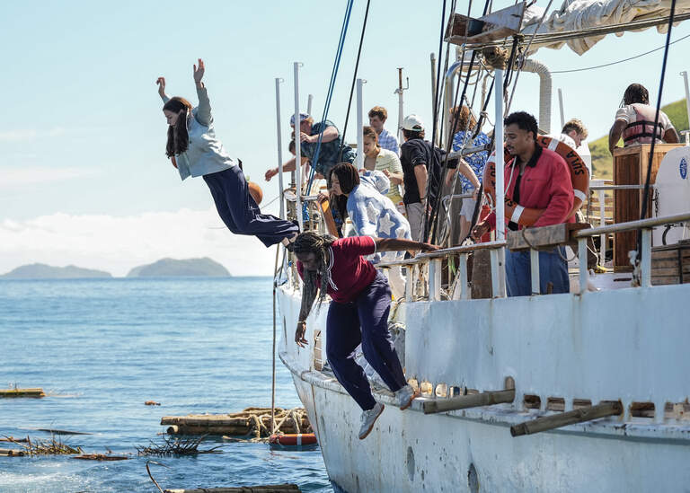 Still from Survivor episode; People leap from a crowded boat into bright blue water as others watch from the deck, creating a lively, adventurous scene on a sunny day.