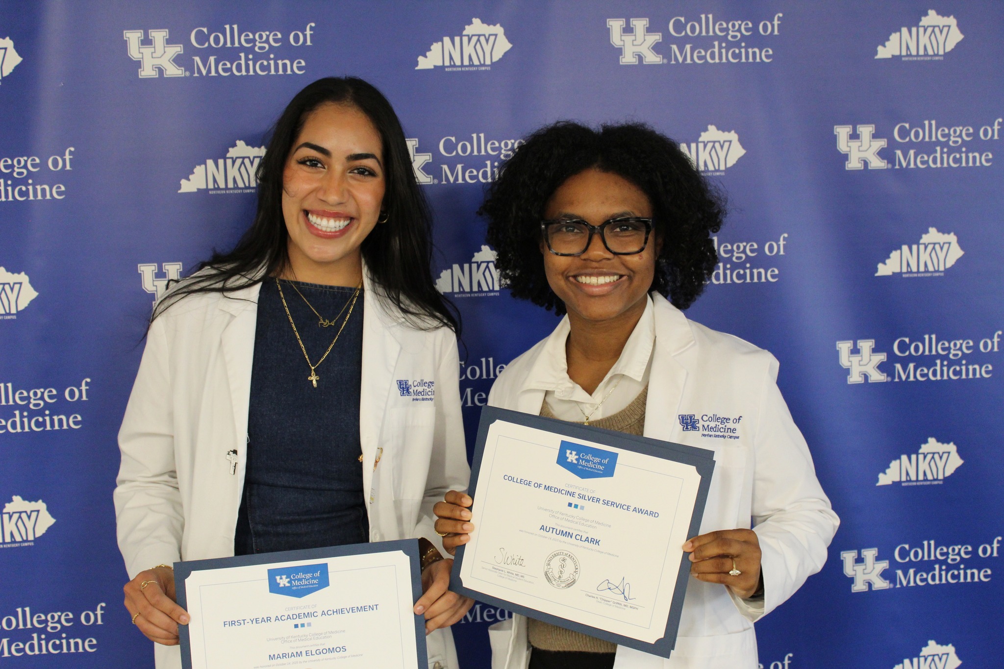 Two awardeeshold certificates and pose for a photo in front of blue backgroudn