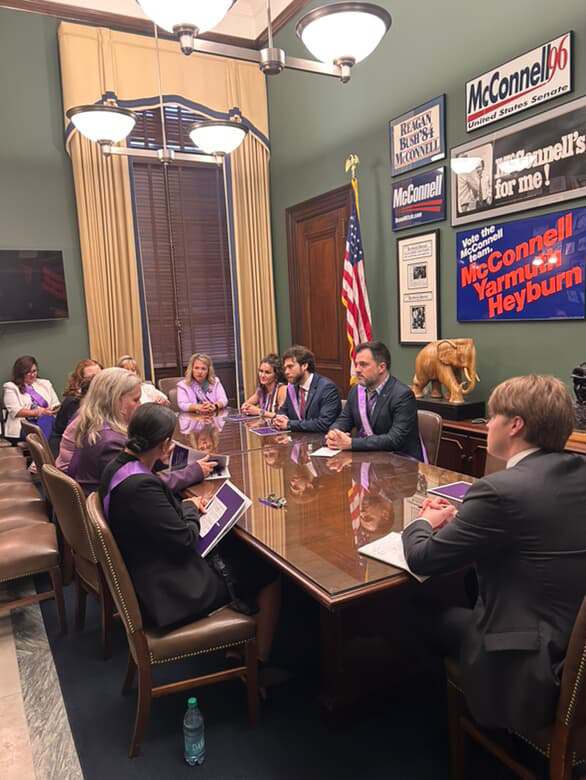 Volunteer advocates sit around a large wooden table in lawmaker's office